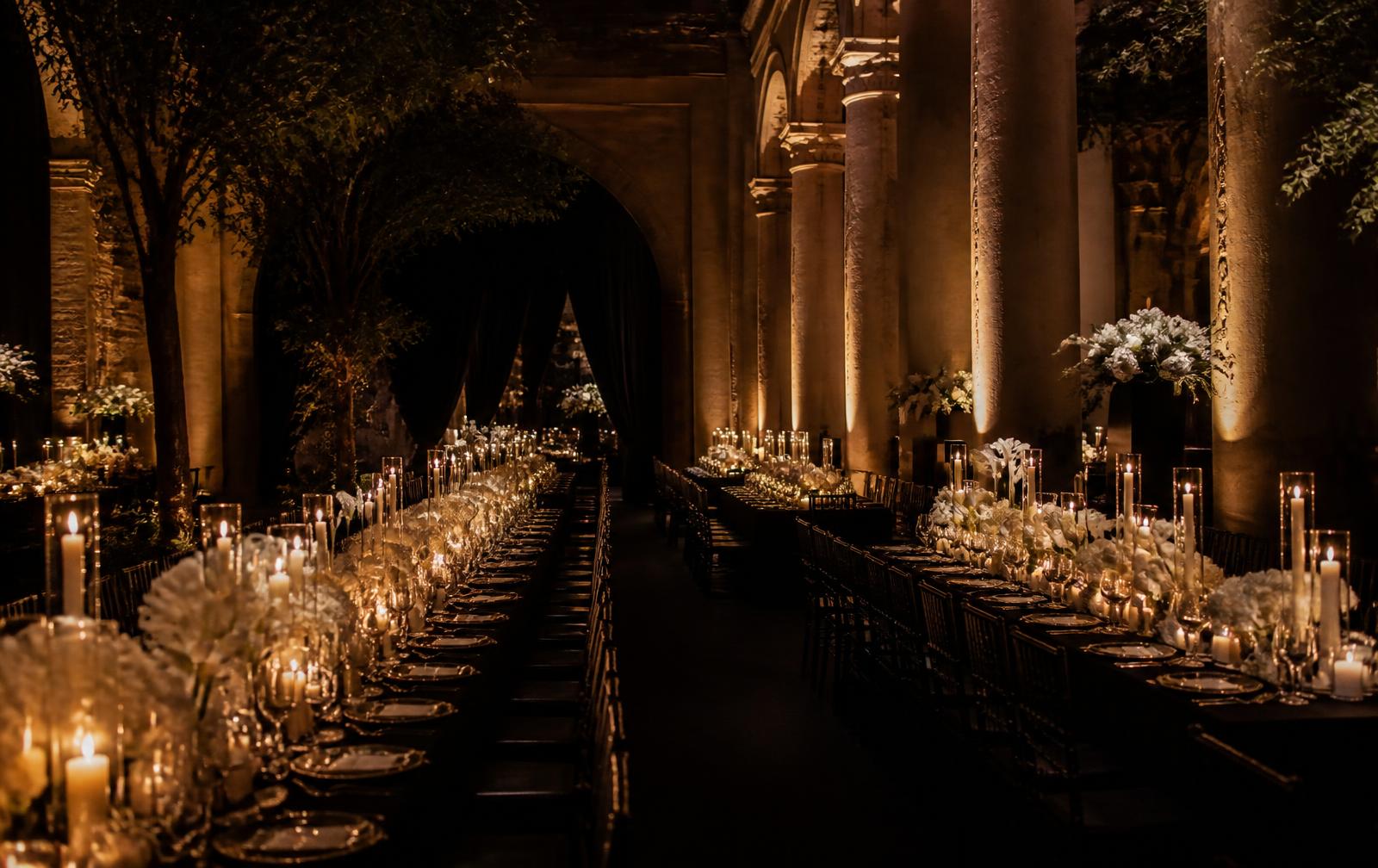 Candlelit banquet hall with long tables, ivory florals and warm gold uplighting